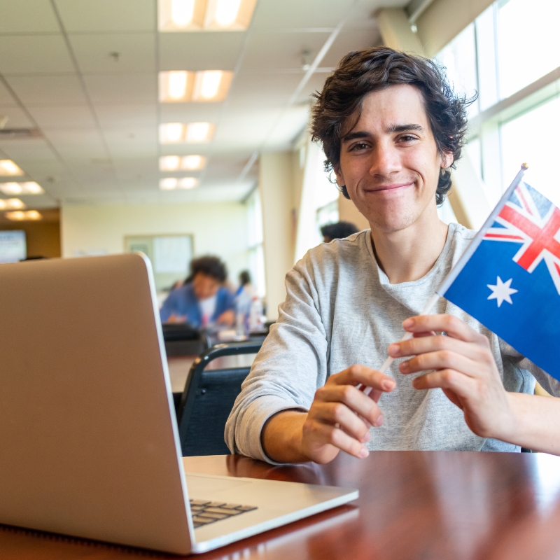 A male student looks very happy to get an Australian visa with the Australian flag in his hand.