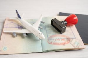 Model airplane, passport, and rubber stamp on an open visa page, symbolising international travel and work visa employer sponsorship requirements.