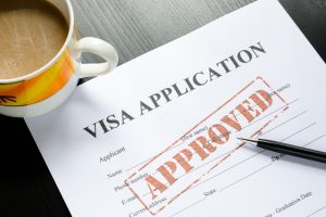 A completed visa application form with an "Approved" stamp, a pen, and a cup of coffee, symbolising success in obtaining a 101 visa.