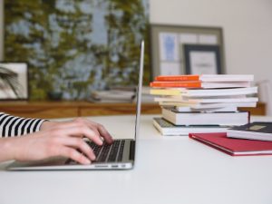 Person typing on laptop beside a stack of books, preparing for the citizenship test in Australia.