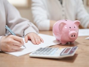 Close-up of hands with a notebook, calculator, and piggy bank, evaluating economic reasons to migrate to Australia.