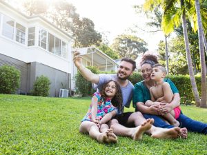 A happy family of four standing in the backyard in Australia, embracing a new life together. Family migration to Australia.